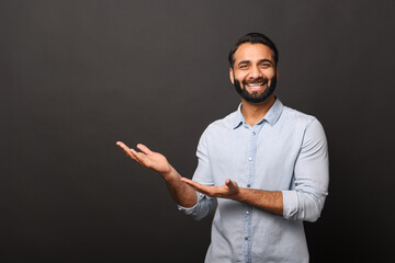 Happy Indian bearded man in casual shirt points hands aside at empty space, hispanic man...