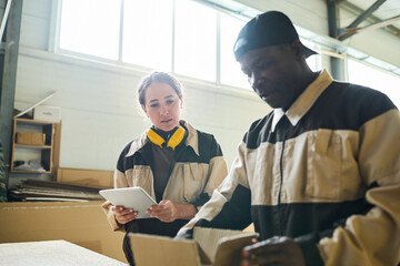 Young woman in uniform using digital tablet while her colleague packing box at table