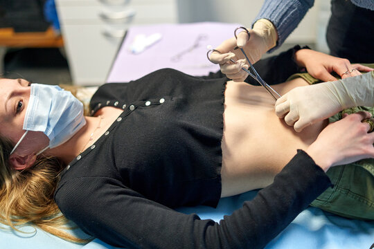 Crop piercer using forceps on belly button of woman
