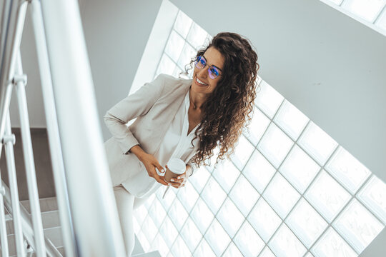 Happy Businesswoman With Frizzy Hair Looking Away Against Wall. Thoughtful Female Professional Is Holding Disposable Cup. She Is Wearing Suit