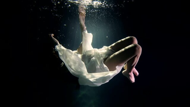 a girl in a white dress under the water mysteriously hangs in the rays of the sun as in a fairy-tale dream