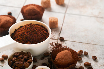 Coffee background. Measuring spoons with ground coffee, beans, cup and sweet chocolate truffles on old tile cracked table background. Food background. Top view with space for your text