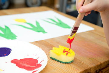 Kid painting with gouache a spring flower. Boy produces colored tulips for mommy. Children's...