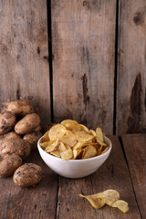 Bowl with potato chips and potatoes on wooden background
