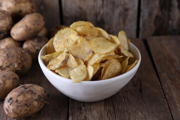 Bowl with potato chips and potatoes on wooden background