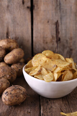 Bowl with potato chips and potatoes on wooden background