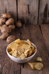 Bowl with potato chips and potatoes on wooden background