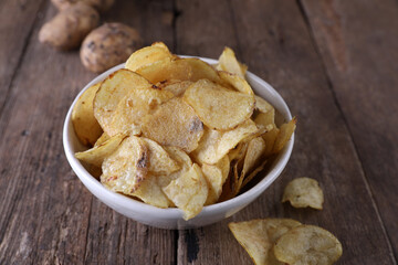 Bowl with potato chips and potatoes on wooden background