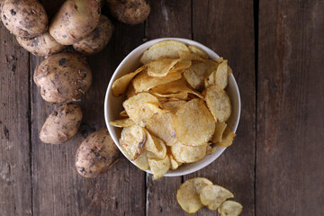 Fototapeta premium Bowl with potato chips and potatoes on wooden background