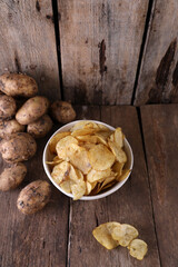 Bowl with potato chips and potatoes on wooden background