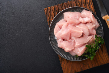 Raw chicken breast sliced or cut pieces on wooden cutting board with herbs and spices on dark...