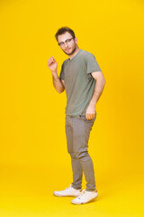 Fototapeta na wymiar Handsome young man in casual wear in glasses posing on yellow background with one hand up. Stylish bearded smart casual look hipster man. Thoughtful young man on yellow background