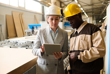 Two engineers in helmet working on digital tablet and controlling the work at furniture factory