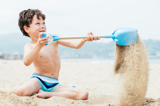 Glad little boy digging sand on beach