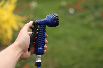 Watering green garden with outdoor hose. hand with hose sprinkle watering plants in the garden. watering lawn or plants on backyard. gardener man with sprinkler in garden