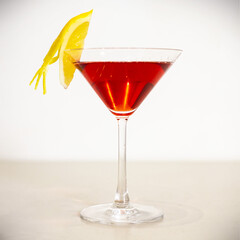 Akafuji cocktail made with vodka, malibu, pomegranate syrup with lemon juice and hint of bitter, glass of red cocktail summer drinks on table plain background