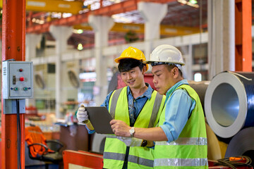 Two Engineers working with tablet check up heavy machine of metal sheet factory