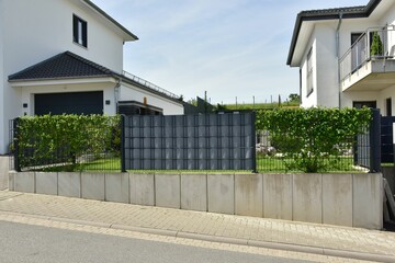 Stahlgitterzaun mit grauer Sichtschutzfolie zwischen Bürgersteig und Wohngrundstück