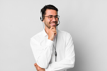 young adult hispanic man smiling with a happy, confident expression with hand on chin. telemarketer concept