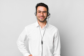 young adult hispanic man smiling happily with a hand on hip and confident. telemarketer concept