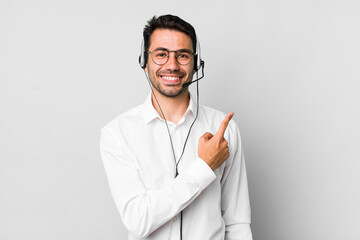 young adult hispanic man smiling cheerfully, feeling happy and pointing to the side. telemarketer concept - obrazy, fototapety, plakaty
