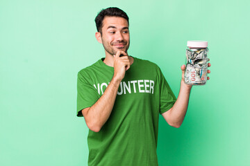 young adult hispanic man smiling with a happy, confident expression with hand on chin. donation...