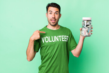 young adult hispanic man feeling happy and pointing to self with an excited. donation concept
