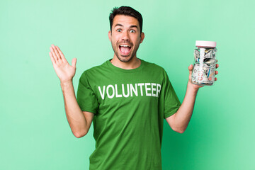 young adult hispanic man feeling happy and astonished at something unbelievable. donation concept