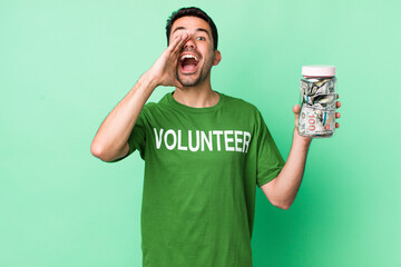 young adult hispanic man feeling happy,giving a big shout out with hands next to mouth. donation...