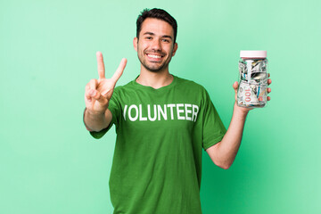 young adult hispanic man smiling and looking friendly, showing number two. donation concept