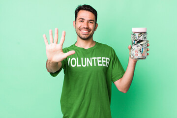 young adult hispanic man smiling and looking friendly, showing number five. donation concept
