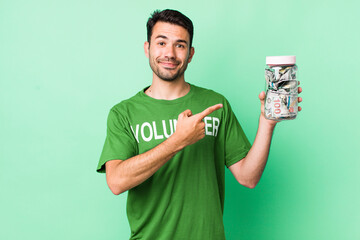 young adult hispanic man smiling cheerfully, feeling happy and pointing to the side. donation...