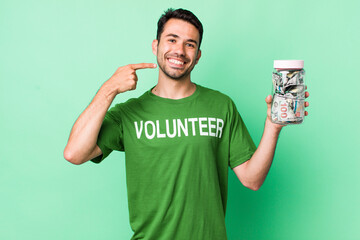 young adult hispanic man smiling confidently pointing to own broad smile. donation concept