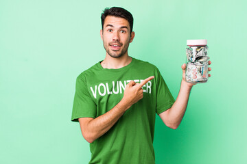 young adult hispanic man looking excited and surprised pointing to the side. donation concept
