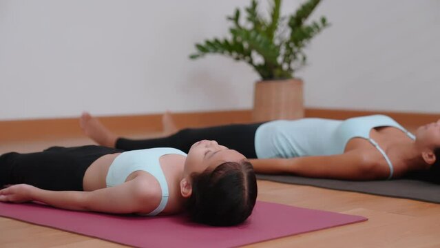 A beautiful asian mother and her little daughter smile while doing yoga together in Savasana Pose or Corpse pose at home. Parents and children's sports and exercises for healthy lifestyle.