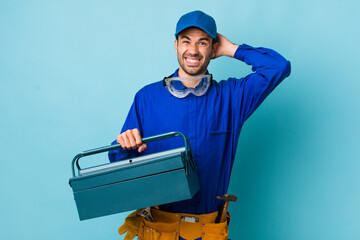young adult hispanic man feeling stressed, anxious or scared, with hands on head. toolbox concept...