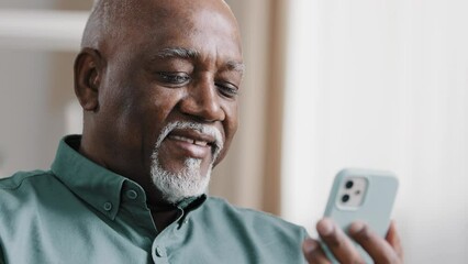 Mature elderly old African 60s biracial man using phone American businessman male grandfather free wi-fi chatting mobile app at home browsing net texting message in smartphone internet technology - Powered by Adobe