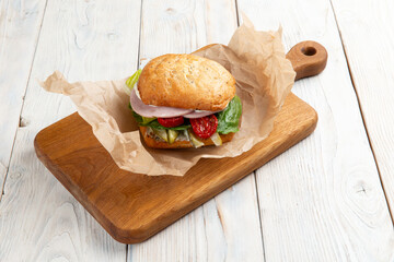 Sandwich with ham sun-dried tomatoes and lettuce on a light background.