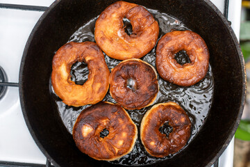 Cooking fresh homemade round donuts in a frying pan. Brown fried doughnuts in boiling oil. Yeast dough products, sweet pastries are prepared on the stove.
