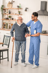 Joyous pensioner moving around the kitchen assisted by his caregiver