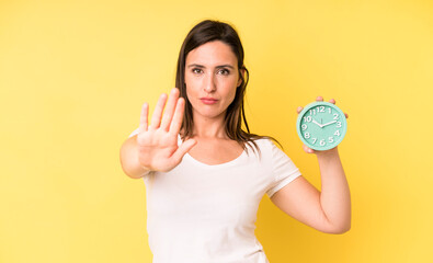 young adult pretty woman looking serious showing open palm making stop gesture. alarm clock concept