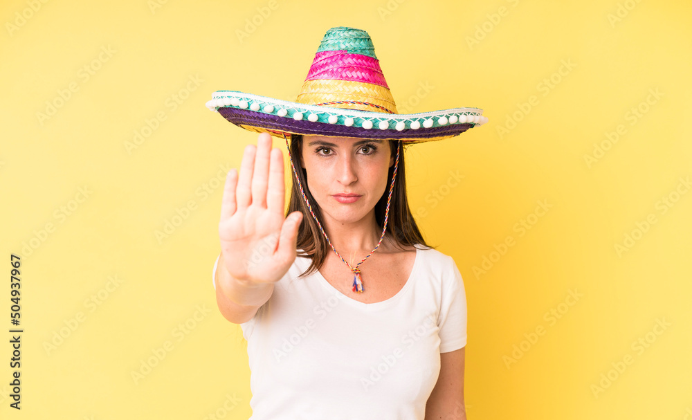 Wall mural young adult pretty woman looking serious showing open palm making stop gesture. mexican hat concept