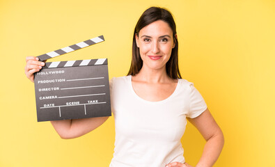 young adult pretty woman smiling happily with a hand on hip and confident. cinema clapper concept