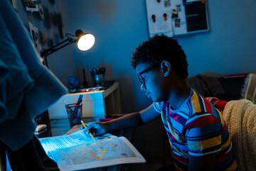 Black boy in eyeglasses doing homework while sitting at table