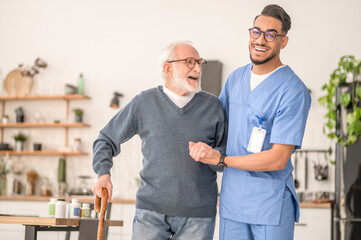 Nurse helping his senior patient to walk with a cane - obrazy, fototapety, plakaty