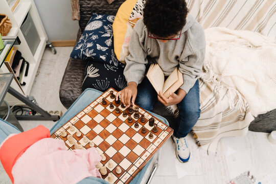 Black boy in eyeglasses playing chess while sitting on sofa
