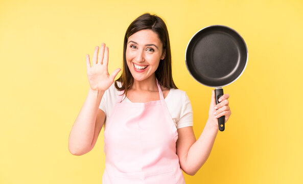 young adult pretty woman smiling happily, waving hand, welcoming and greeting you. cooking at home chef concept