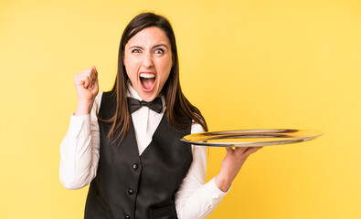 young adult pretty woman shouting aggressively with an angry expression. waiter and tray concept