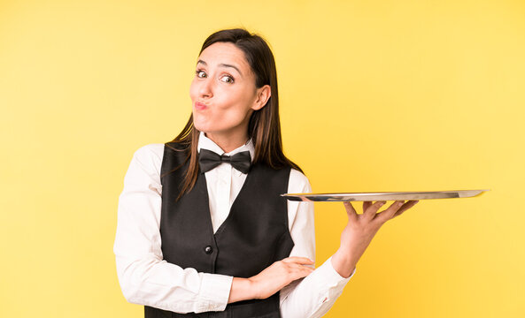 young adult pretty woman shrugging, feeling confused and uncertain. waiter and tray concept