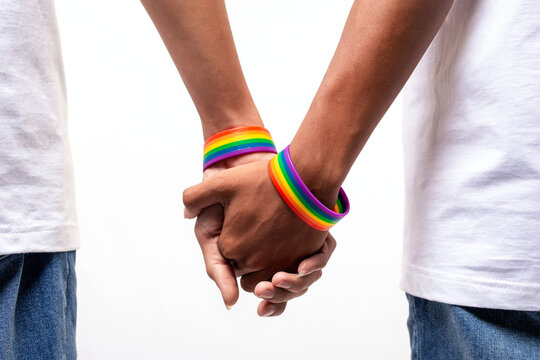 Male couple wearing gay pride rainbow awareness wristbands holding hands on white. lgbt, same-sex relationships and homosexual concept